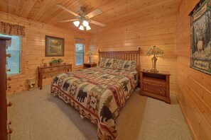 Un dormitorio de estilo cabaña acogedor, con techo de madera, una cama con colcha estampada, dos mesitas de noche con lámparas y una ventana con persianas.