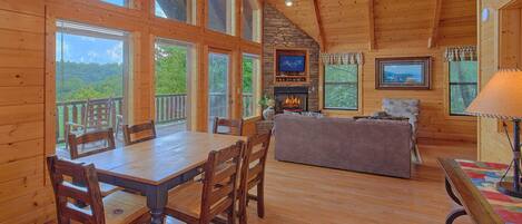 A wooden interior with a dining table, chairs, a sofa, and a fireplace.