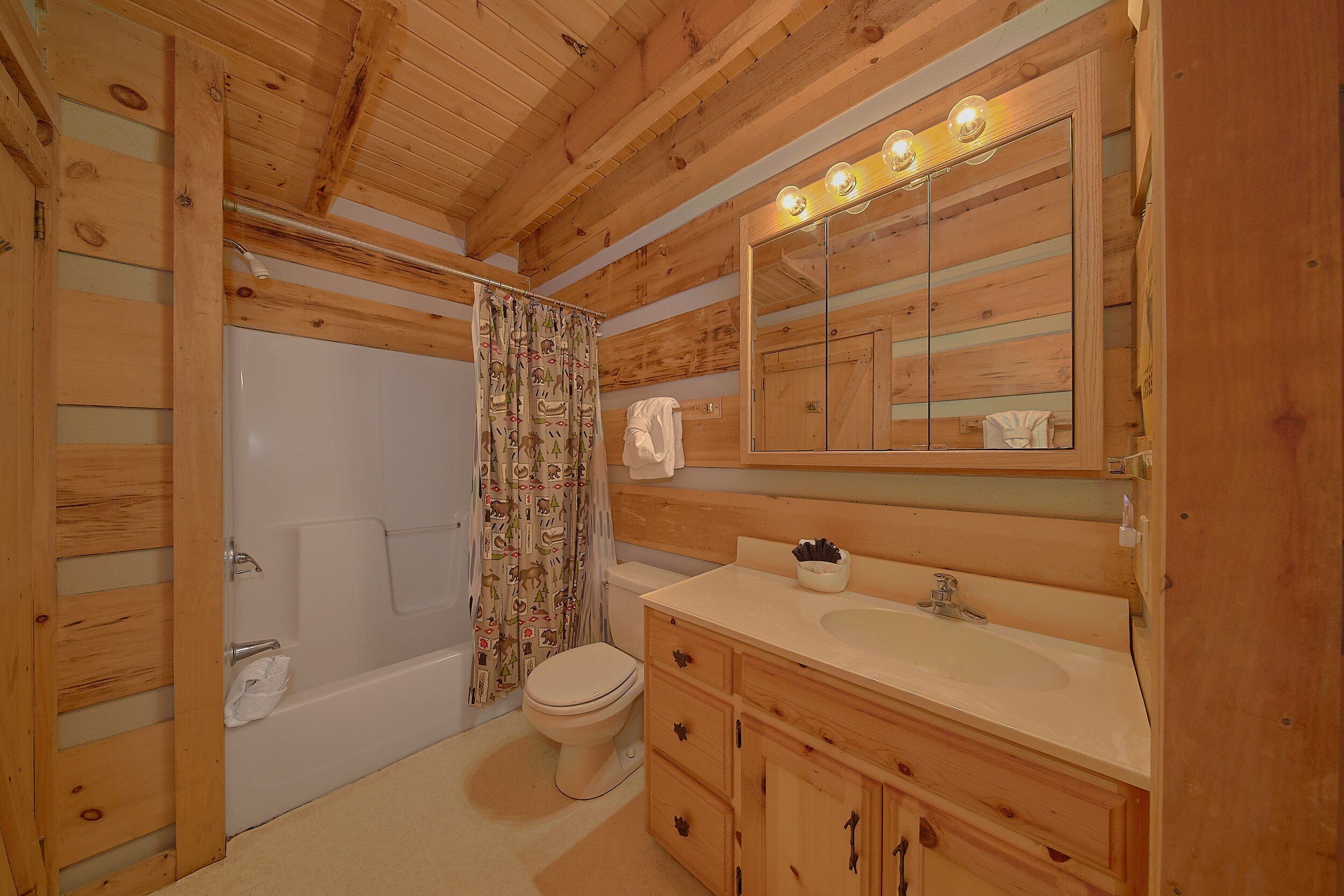 A wooden cabin bathroom with a bathtub, toilet, and vanity with a mirror.