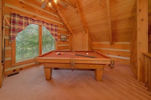 A wooden interior with a pool table, plaid curtains, and a window with blinds. - Moose Tracks | Mtn Views, Game Room, Resort Pool, Pet Friendly, Fireplace + Free Attraction Tickets (Wears Valley)