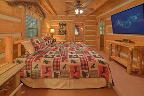 A log cabin bedroom with a bed, a television, and a ceiling fan.