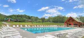 A swimming pool with lounge chairs, a wooden building, and a green landscape. - Moose Tracks | Mtn Views, Game Room, Resort Pool, Pet Friendly, Fireplace + Free Attraction Tickets (Wears Valley)