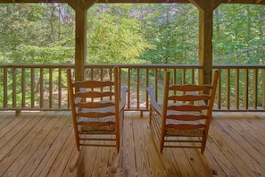 A wooden deck with two chairs facing a railing, overlooking a forested area. - Moose Tracks | Mtn Views, Game Room, Resort Pool, Pet Friendly, Fireplace + Free Attraction Tickets (Wears Valley)