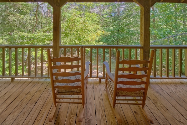 A wooden deck with two chairs facing a railing, overlooking a forested area.