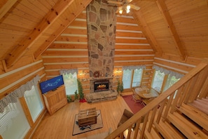 A log cabin interior with a stone fireplace, wooden furniture, and a television.