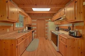 A compact kitchen with wooden cabinets, a central island, a stove, and a refrigerator. - Moose Tracks | Mtn Views, Game Room, Resort Pool, Pet Friendly, Fireplace + Free Attraction Tickets (Wears Valley)