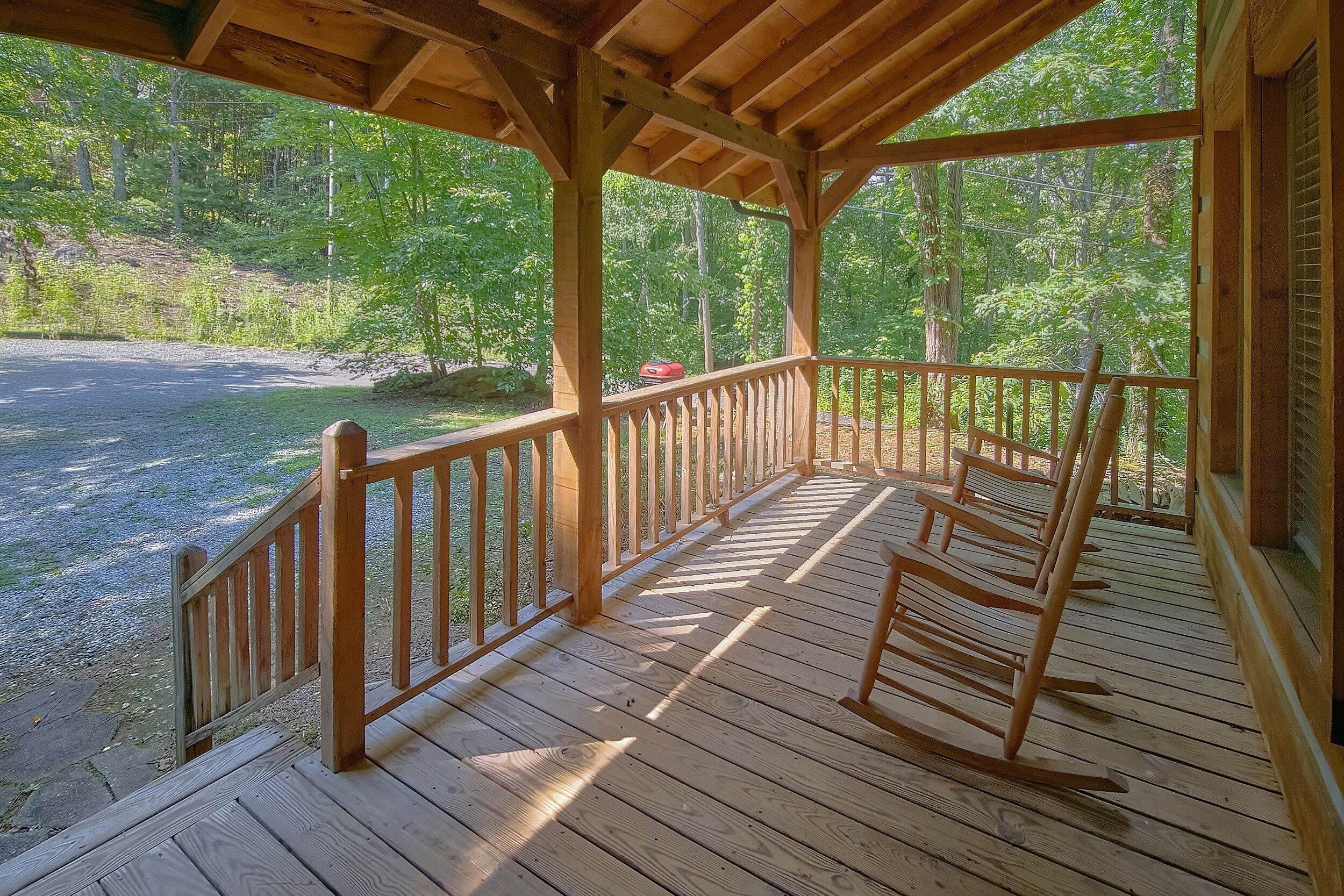 A wooden deck with a railing, overlooking a gravel area and a forested landscape.