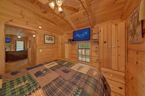 A cozy cabin interior with a large bed, wooden walls, a television, and a window with a view. - Camping Under the Stars Cabin Rental (Wears Valley)
