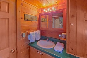 A wooden bathroom with a sink, mirror, and two towel hooks labeled 'BATH'. - Camping Under the Stars Cabin Rental (Wears Valley)