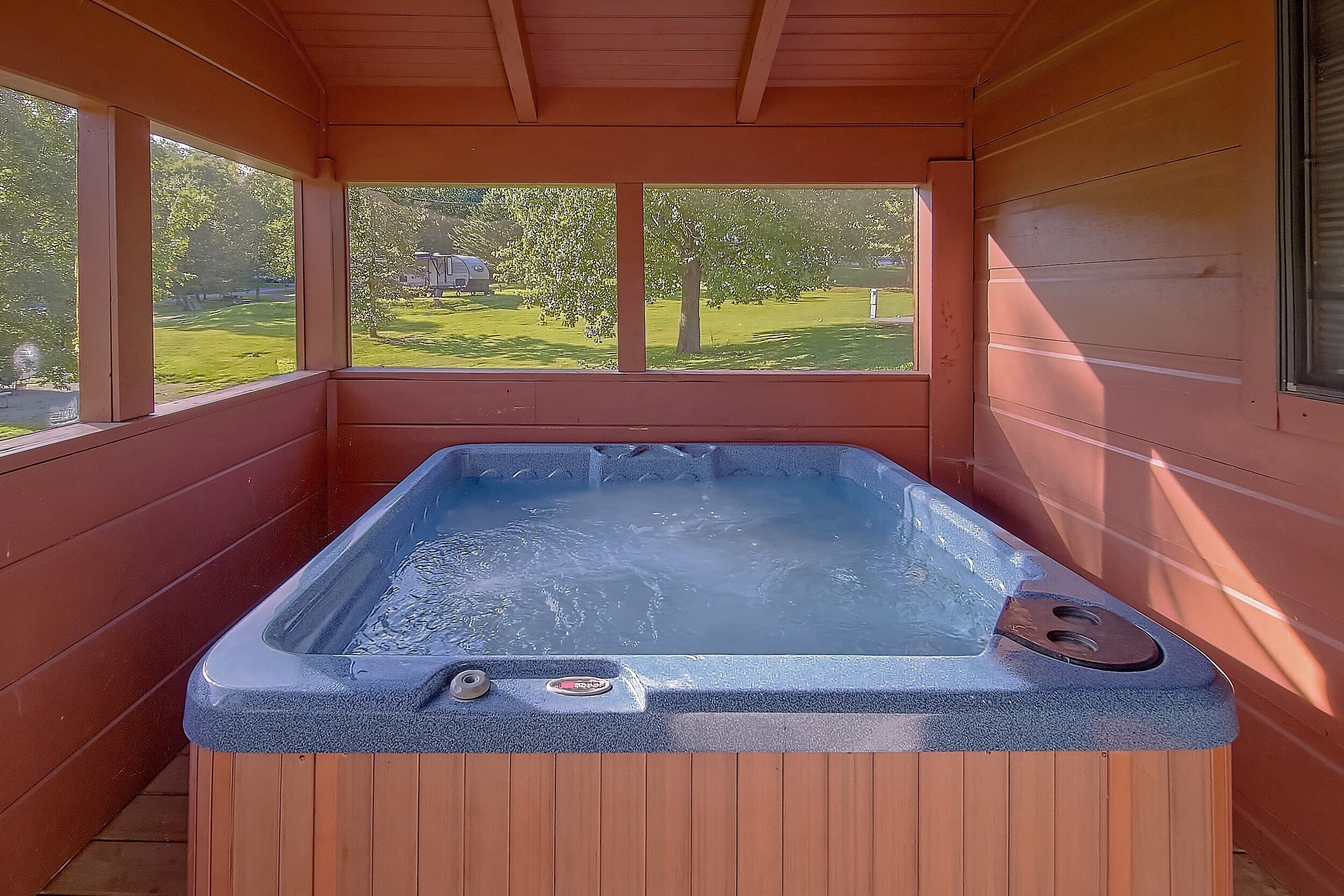 A hot tub in a wooden cabin with a view of a green landscape.