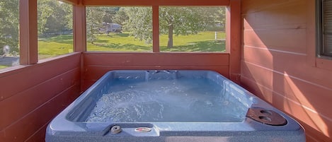 A hot tub in a wooden cabin with a view of a green landscape.
