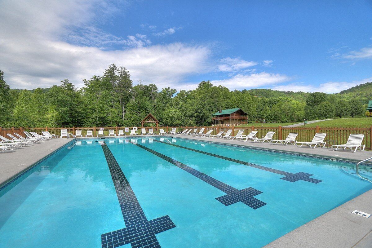 A swimming pool with multiple lanes, surrounded by lounge chairs and a wooden fence.