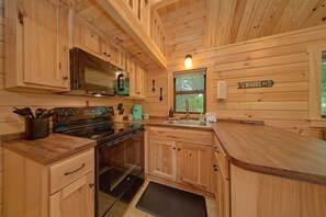 Uma cozinha rústica em estilo cabana, com micro-ondas, fogão e pia.