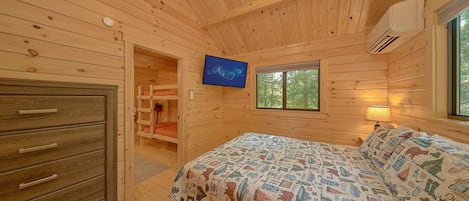 A wooden cabin bedroom with a bed, dresser, TV, and a window.