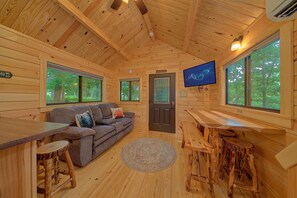 Ein gemütliches Blockhaus-Interieur mit einer Couch, einem Esstisch und einem an der Wand befestigten Fernseher.