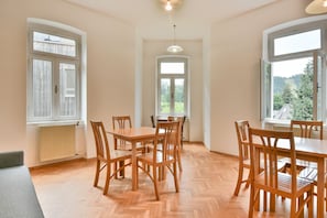 Uma área de refeições com uma mesa grande e cadeiras, grandes janelas com vista para o verde, e um lustre.