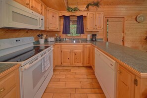 A kitchen with wooden cabinets, a microwave, a stove, and a sink. - Southern Charm Cabin Rental (Wears Valley)