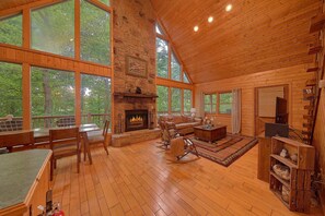 A spacious living room with a fireplace, wooden flooring, and large windows offering a view of the outdoors. - Southern Charm Cabin Rental (Wears Valley)