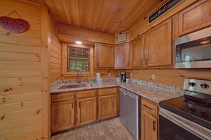 A wooden cabin interior with a kitchen featuring wooden cabinets, a granite countertop, a stainless steel refrigerator, and a built-in oven. - Run to the Hills | Mtn Views, Hot Tub, Resort Pool + Free Attraction Tickets (Wears Valley)