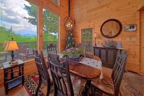 A wooden interior with a dining table and chairs, a Christmas tree, and a view of greenery outside. - Run to the Hills | Mtn Views, Hot Tub, Resort Pool + Free Attraction Tickets (Wears Valley)