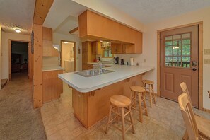 A kitchen with a central island, wooden stools, and a door with a window. - Misty Cove Cabin Rental (Wears Valley)