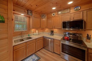 A kitchen with wooden cabinets, a stainless steel dishwasher, a microwave, a stove, and a coffee maker. - Eagle's Nest | Mtn Views, Hot Tub, Fireplace + Free Attraction Tickets (Wears Valley)