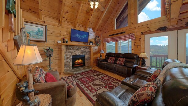 A cozy log cabin interior with a fireplace, leather furniture, and a television.