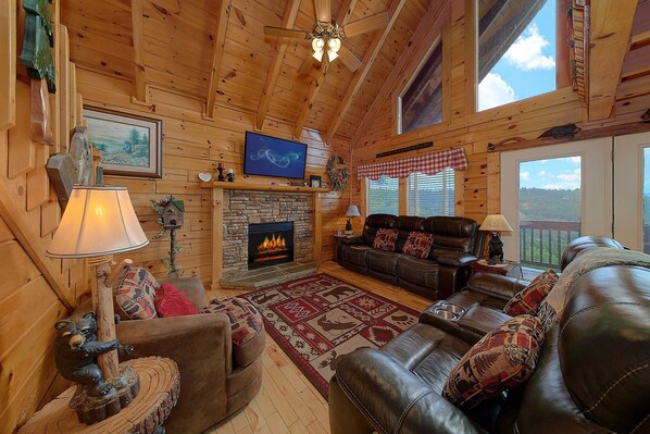 A cozy log cabin interior with a fireplace, leather furniture, and a television.