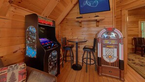 A wooden interior with arcade machines, a television, and a small table with chairs.