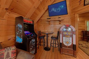 A wooden interior with arcade machines, a television, and a small table with chairs.