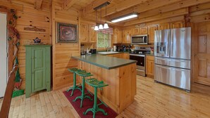 A wooden cabin interior with a kitchen featuring a refrigerator, microwave, stove, and bar stools.