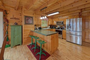 A wooden cabin interior with a kitchen featuring a refrigerator, microwave, stove, and bar stools.