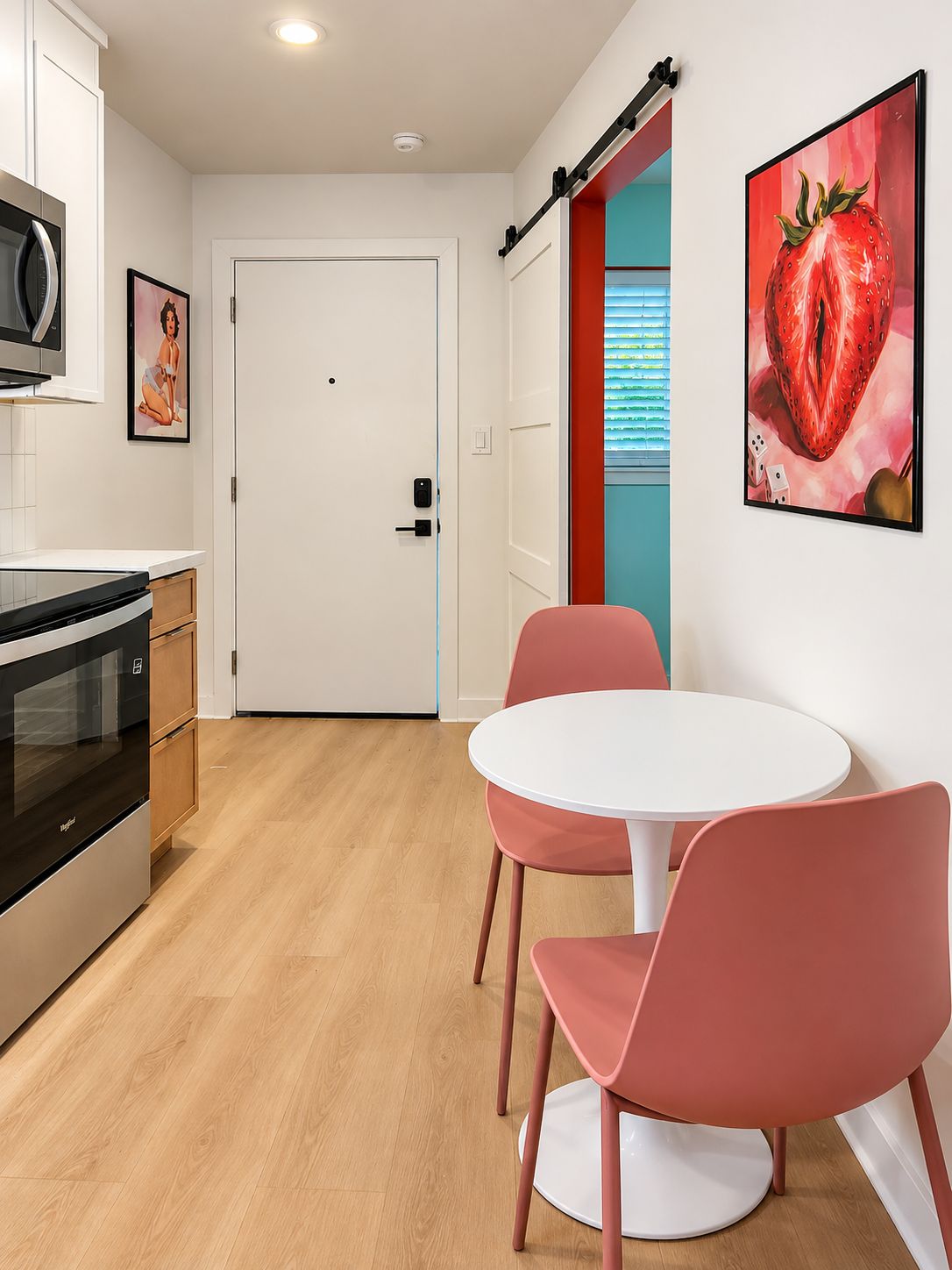 Une cuisine moderne équipée d’un four à micro-ondes, d’un four traditionnel et de placards, avec une porte blanche et un coin repas comprenant une table ronde et des chaises roses.