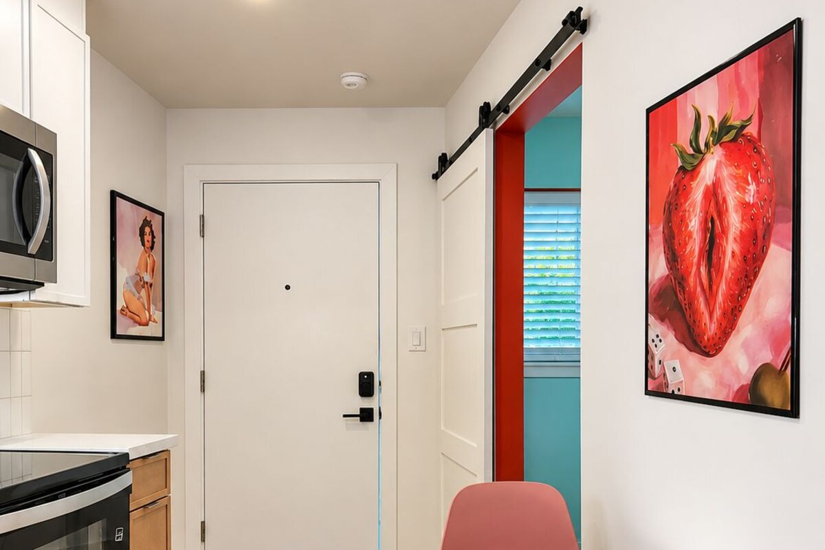 A modern kitchen with a microwave, oven, and cabinets, a white door, and a dining area with a round table and pink chairs.