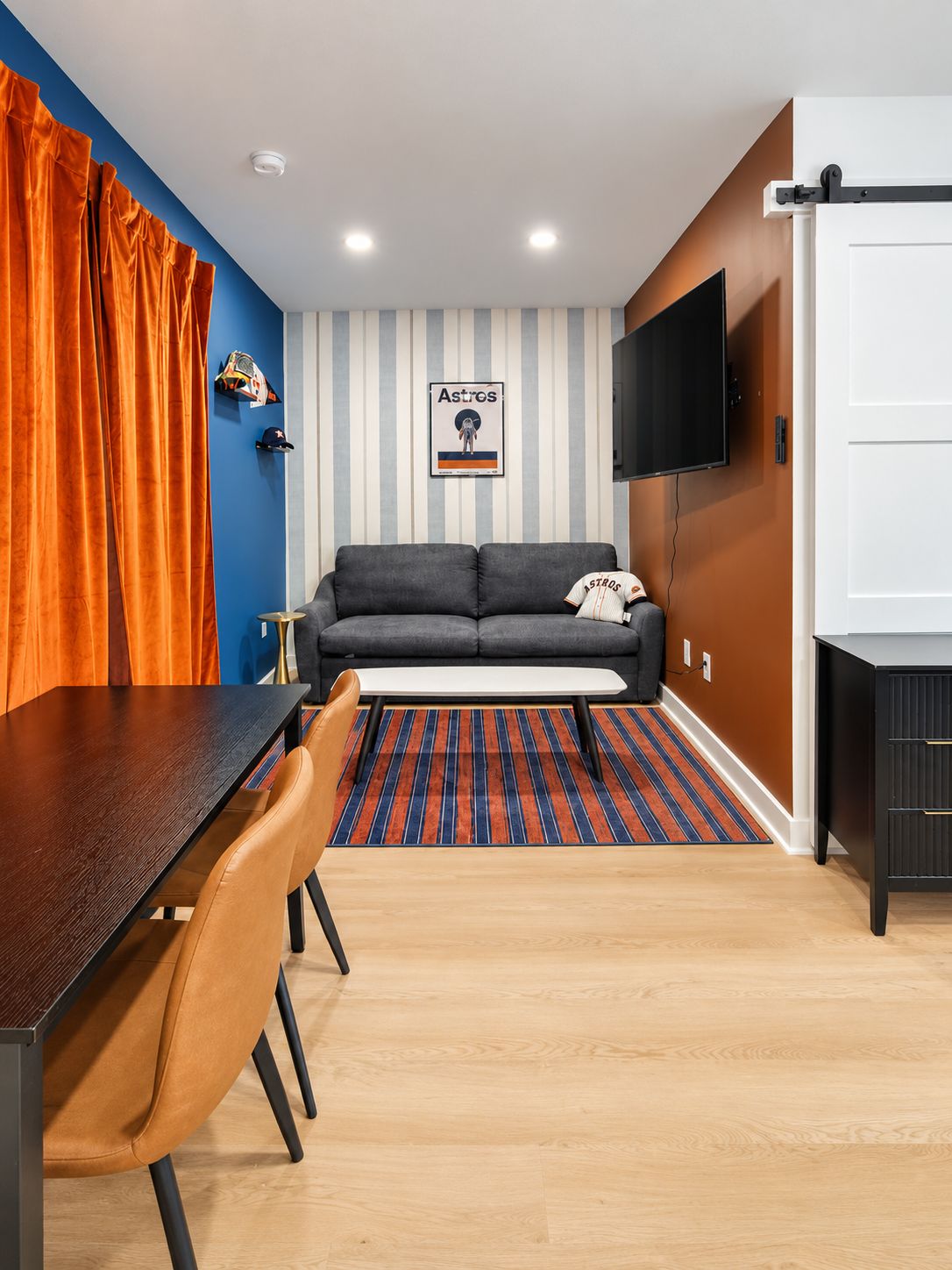 A modern living room with a sofa, a flat-screen TV, a dining table with chairs, and a striped rug.