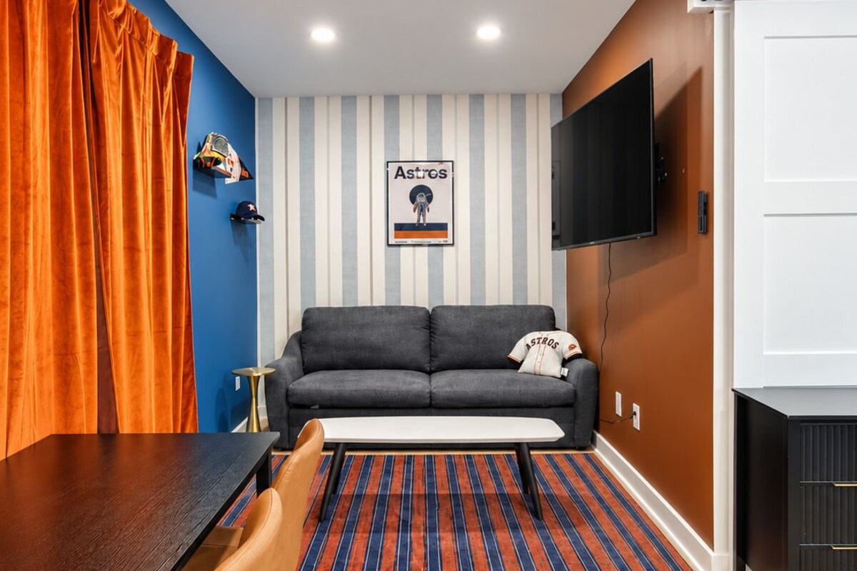 A modern living room with a sofa, a flat-screen TV, a dining table with chairs, and a striped rug.