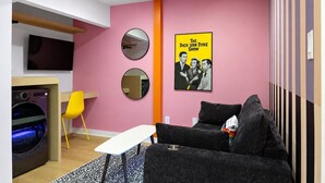 Una sala de estar moderna con una pared rosa, un sofá, una mesa de centro, un televisor y un cartel de 'The Dick Van Dyke Show'.