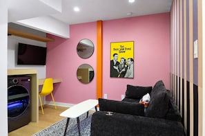 A modern living room with a pink wall, a sofa, a coffee table, a TV, and a poster of 'The Dick Van Dyke Show'. - The Montage (Houston)