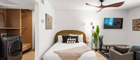 A modern bedroom with a bed, a ceiling fan, a TV, a washing machine, and a dining area.