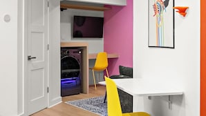Un interior moderno con piso de madera, una puerta blanca, un comedor con mesa y sillas, y una obra de arte colgada en la pared.
