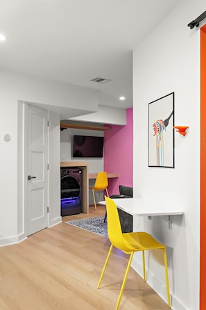 A modern interior with a wooden floor, a white door, a dining area with a table and chairs, and a wall-mounted artwork. - The Montage (Houston)