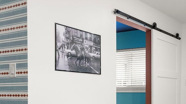 Una habitación con un escritorio blanco, una silla marrón, una fotografía blanco y negro en la pared y una puerta corrediza que da a otra habitación.
