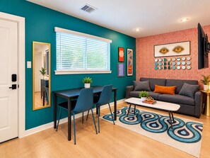 Una sala de estar moderna con paredes verde azulado, un sofá gris, una mesa de centro y un comedor con sillas y una mesa.