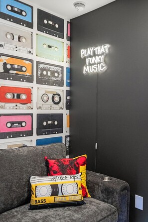 Una habitación con una pared decorada con varias cintas de cassette y un letrero de neón que dice 'PLAY THAT FUNKY MUSIC'.