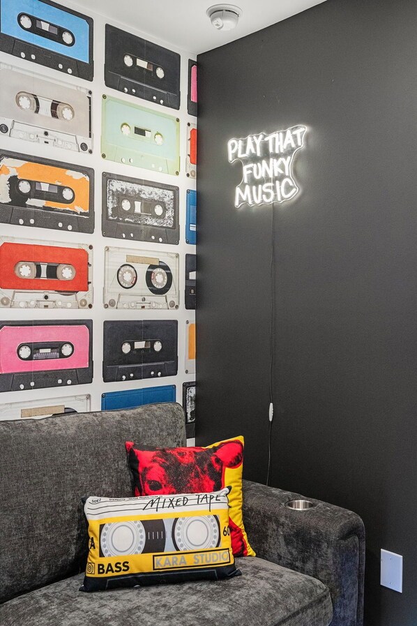 A room with a wall decorated with various cassette tapes and a neon sign that reads 'PLAY THAT FUNKY MUSIC'. - The Montage (Houston)