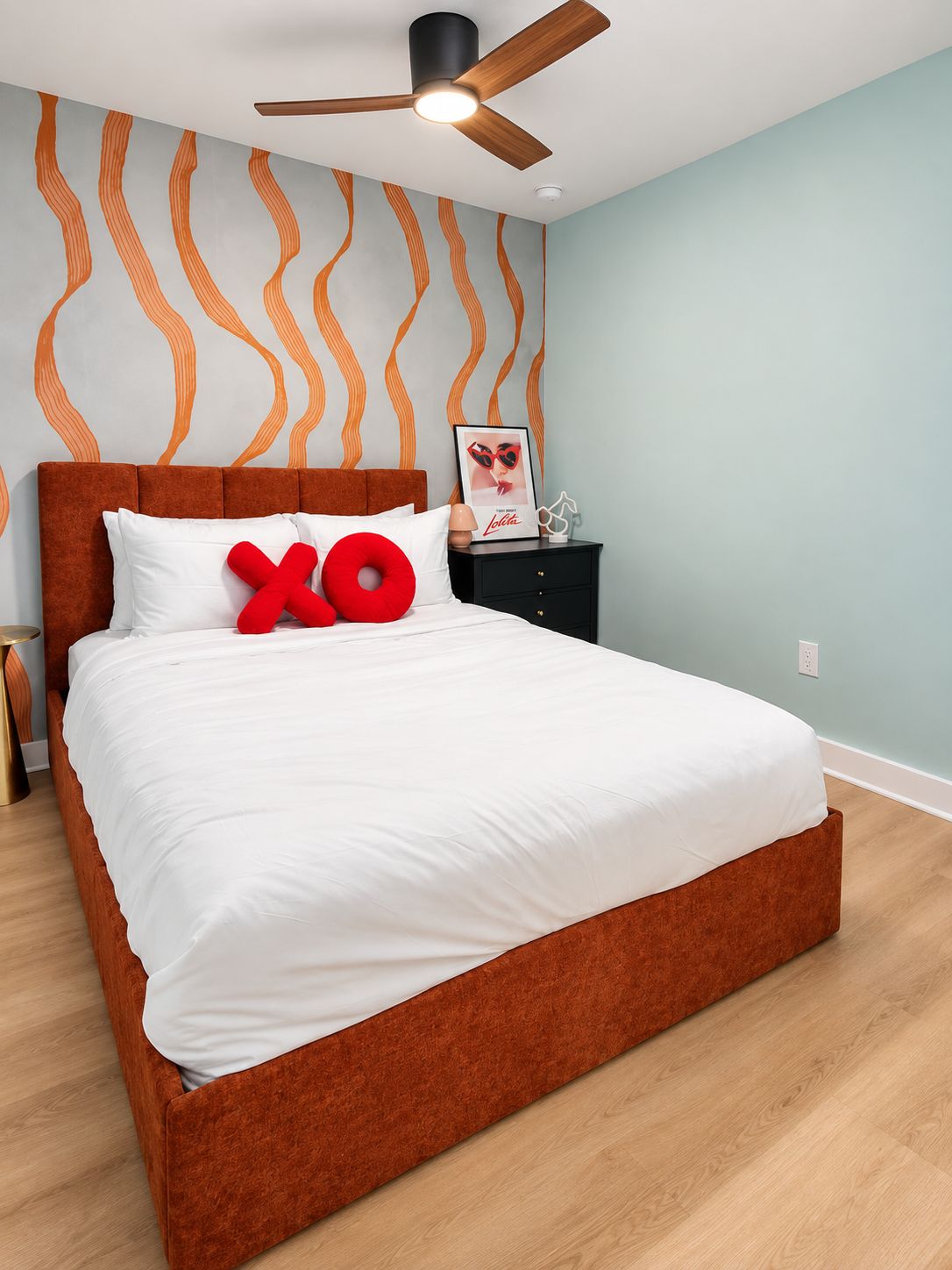 Un dormitorio con una cama grande, un ventilador de techo, una mesita de noche y una pared con un diseño ondulado.