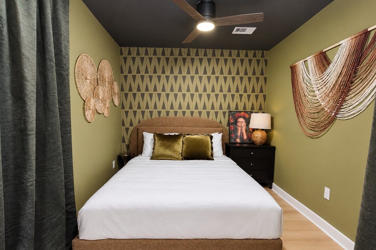 A bedroom with a bed, a nightstand, a wall-mounted fan, and a patterned wall.