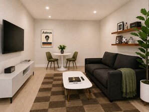 A modern living room with a flat-screen TV, a sofa, a coffee table, and a dining area with two chairs.