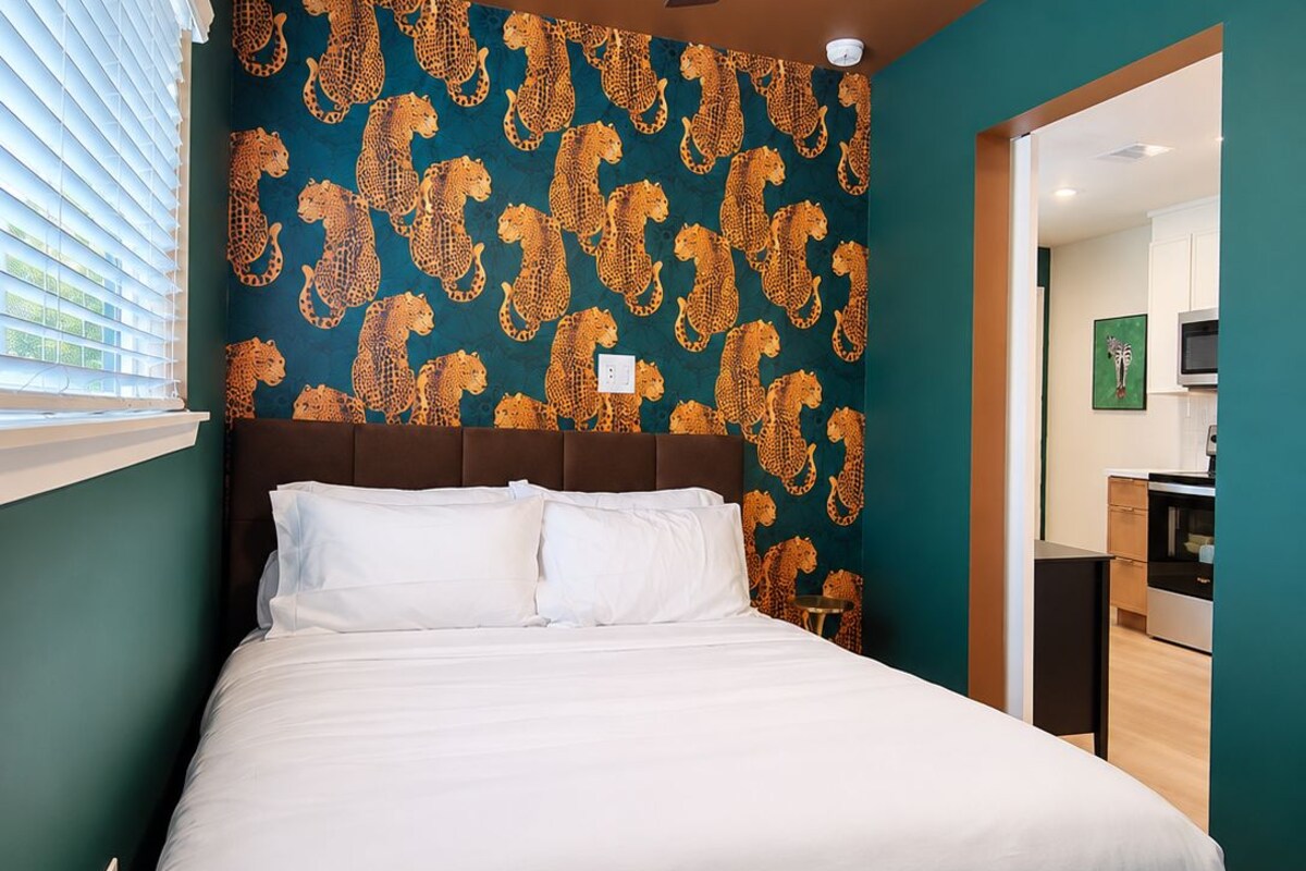 A bedroom with a bed, a ceiling fan, and a wall with a leopard print pattern.