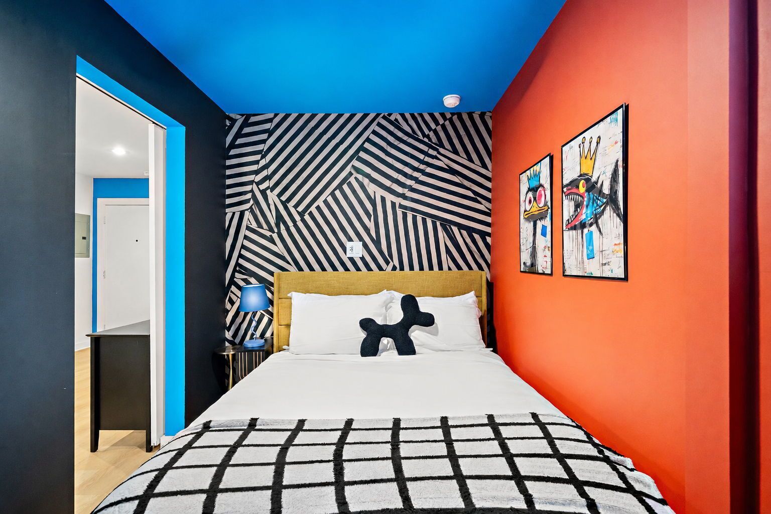 A modern bedroom with a geometric patterned wall, a bed with a black and white checkered bedspread, and two framed artworks on the wall.